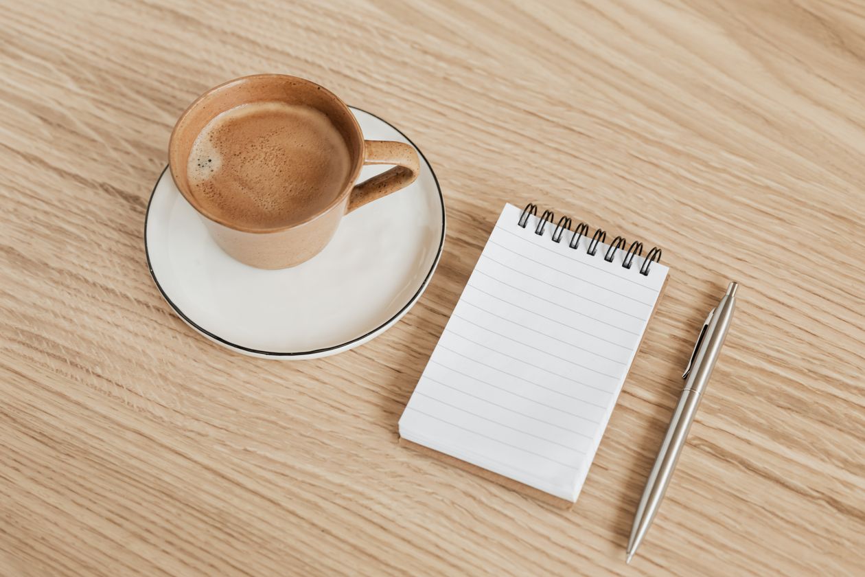 Notebook, pen, and coffee on a wooden desk for study